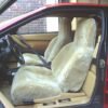 The image shows the interior of a classic Ferrari Testarossa. The car has tan leather seats and a wooden dashboard. The seats are covered with sheepskin seat covers.