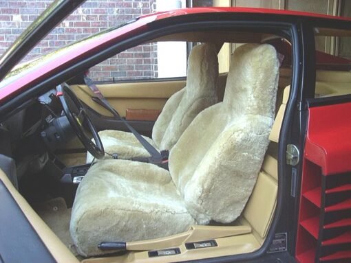 The image shows the interior of a classic Ferrari Testarossa. The car has tan leather seats and a wooden dashboard. The seats are covered with sheepskin seat covers.