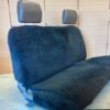 a black sheepskin seat cover for a car's back seat. It covers both the seat and the backrests.