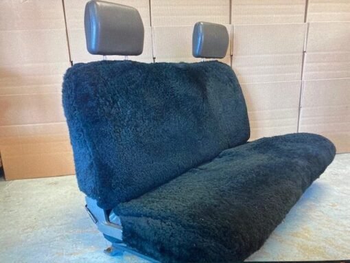 a black sheepskin seat cover for a car's back seat. It covers both the seat and the backrests.